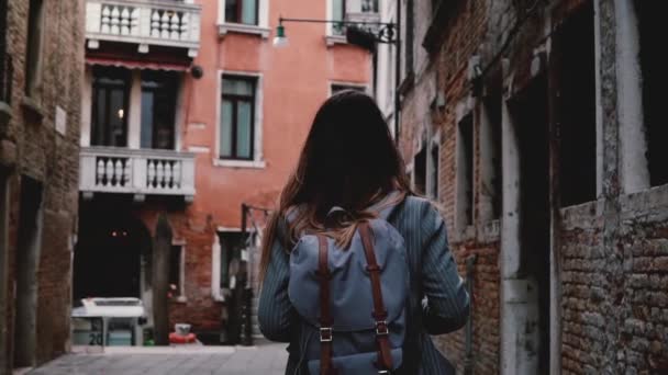 Κάμερα ακολουθεί νεαρό θηλυκό τουριστών με σακίδιο περπατώντας όμορφη αρχαία πόλη σκοτεινό δρόμο σε Βενετία αργή κίνηση — Αρχείο Βίντεο