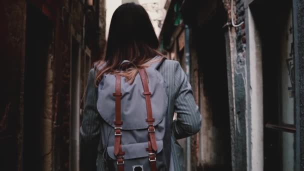 Venedik, İtalya, ağır çekimde karanlık cadde boyunca yürüyüş şık takım elbise giymiş sırt çantası ile görünüm işkadını geri. — Stok video