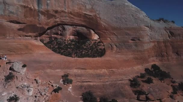 Drone flying away from tourist couple standing in famous Arches rock formation in sunny Arizona mountain national park. — Stock Video
