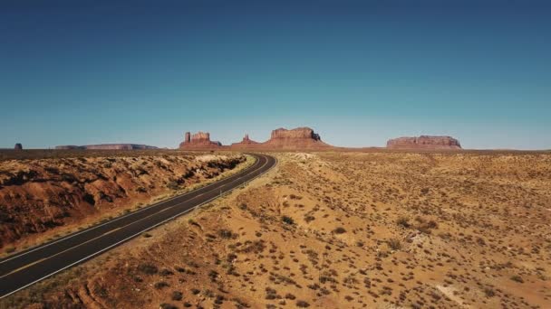 Drone voando à esquerda acima do deserto de arenito vazio rodovia virar em Monuments Valley, Arizona com montanhas planas épicas . — Vídeo de Stock