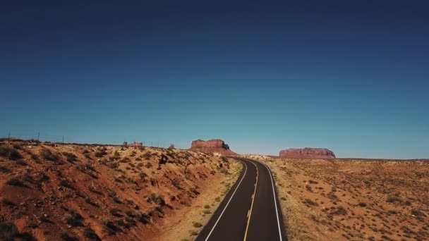 Беспилотник летит вправо над пустынной дорогой и скалами Долины Монументов в США с ясным голубым небом . — стоковое видео