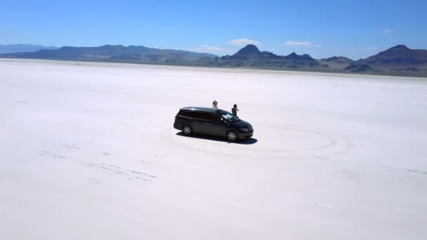 Hisnande antenn skott av glada par med armar öppna i minibuss bil mitt Bonneville salt lake öknen. — Stockvideo