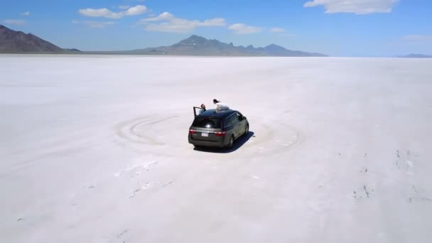 Drone spinning around excited couple kissing on silver minivan car in the middle of amazing Bonneville salt lake desert. — Stock Video