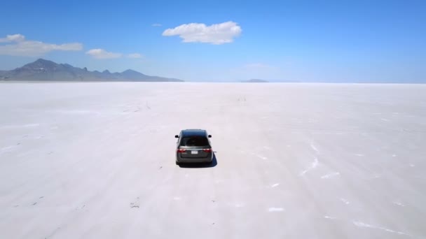 次の息をのむボンネビル塩湖砂漠の真ん中で山に向かって銀ミニバン車ドローン. — ストック動画