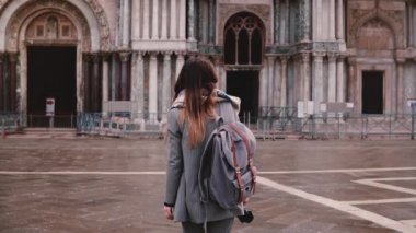 Venedik, İtalya, ağır çekimde güzel San Marco Katedrali doğru yürüyen sırt çantası ile kadın turist kamera izler.