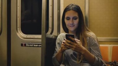 Mutlu rahat güzel bin yıllık kız videoları online smartphone app ve gülümseyen izlerken metro tren oturan.