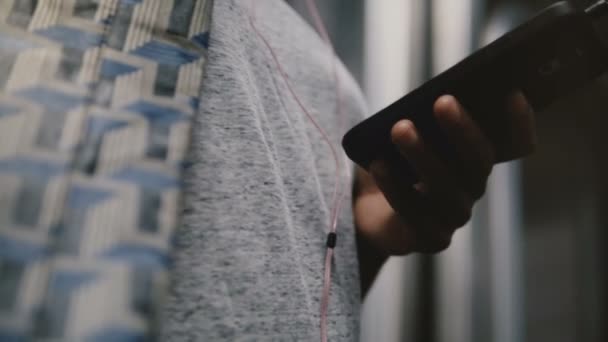 Beau gros plan des mains féminines tenant smartphone avec écouteurs, femme écoutant l'application de musique en dehors en ligne . — Video