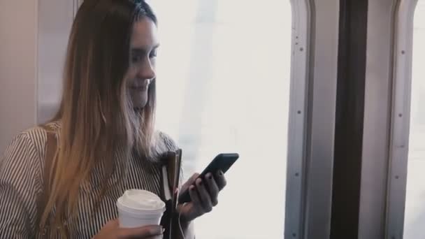 Feliz relajado atractiva chica milenaria en un tren subterráneo mirando el teléfono inteligente utilizando mensajero en la puerta de entrada — Vídeos de Stock