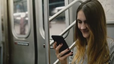 Sosyal ağlar üzerinde smartphone uygulaması kullanarak ve gülümseyen metro tren oturan mutlu çekici bin yıllık freelancer kız. Başarılı genç işkadını haberciler kullanarak arkadaşlarınızla sohbet.