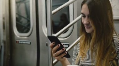 Mutlu çekici emin işkadını metro tren smartphone ve gülümseyen online hareket eden yazıhane app kullanarak.