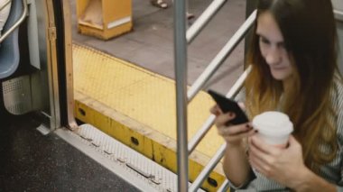 Yüksek açı kamera çekici genç Avrupa kadın metro tren smartphone, kullanarak araç kapıları platforma kapanış.