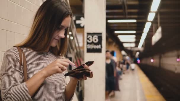 Όμορφη νεαρή γυναίκα σχετικά με την πλατφόρμα τραίνων του μετρό κρατώντας smartphone και πραγματοποίηση αγοράς σχετικά με τις αγορές σε απευθείας σύνδεση app από το πορτοφόλι. — Αρχείο Βίντεο