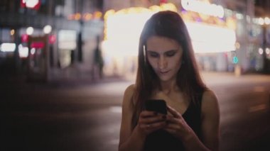 Mutlu beyaz genç yerel kadın koyu New York gece sokak gülümseyen ın smartphone uygulama kullanarak atmosferik orta atış.