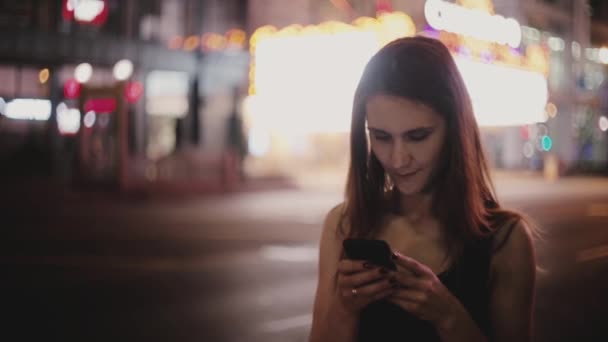 ニューヨークのストリートの暗い笑顔でスマート フォンのアプリを使用して周りを見て幸せなヨーロッパ ローカル女性の美しいミディアム ショット 陽気な千年美少女外オンラインの友達とチャット — ストック動画
