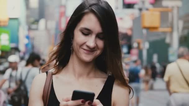 Happy relaxed beautiful millennial girl stands in New York street looking at smartphone using shopping app smiling. — Stock Video