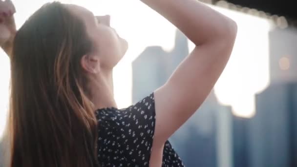 Back view beautiful Caucasian woman touching long flying hair with both hands, looking right at Manhattan city skyline. — Stock Video