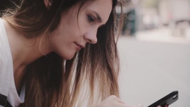 Serious hermosa chica milenaria local sentado fuera en la calle utilizando teléfono inteligente aplicación de oficina móvil buscando centrado — Vídeos de Stock