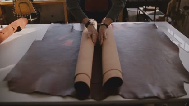 Ovanifrån manliga händer spred sig en stor bit av brunt läder material på ett stort bord i en modern tillverkning verkstad. — Stockvideo