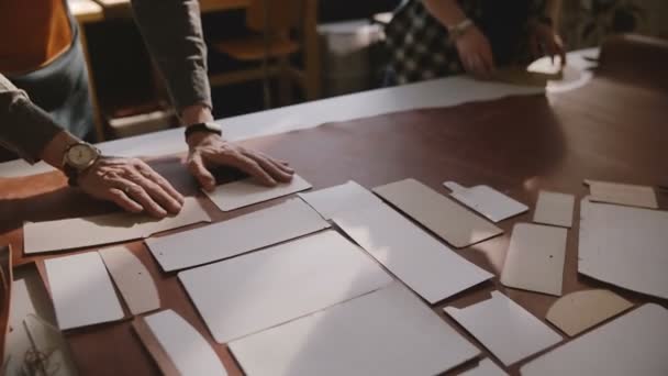 Vista dall'alto di due artigiani professionisti che collaborano in un laboratorio di produzione mettendo modelli di taglio su un pezzo di pelle . — Video Stock