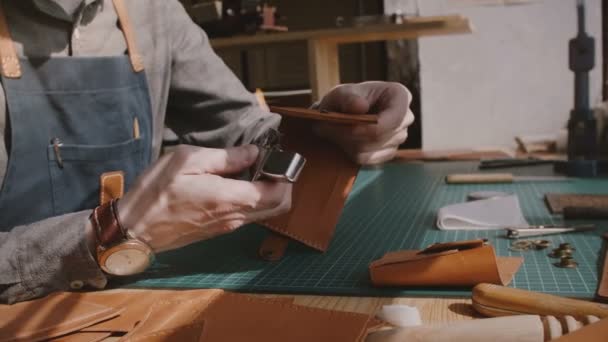 Nahaufnahme von professionellen männlichen Handwerkerhänden, die handgefertigte Ledergeldbörsenränder mit Feuer aus wenig Feuerzeug veredeln. — Stockvideo