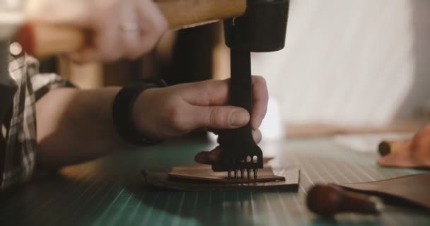 Primer plano de las manos femeninas haciendo agujeros en una pequeña pieza de cuero en una mesa con herramienta de perforación profesional y martillo . — Vídeos de Stock