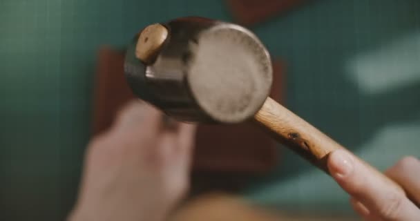 Nahaufnahme kurze Fokusaufnahme von oben, wie professionelle weibliche Hände Löcher in ein kleines Stück Leder schlagen und mit dem Hammer schwingen. — Stockvideo