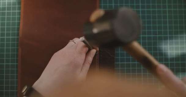 Close-up top shot van professionele vrouwelijke handen met een ring maken van gaten in stukje leer met hamer en punch bekijken. — Stockvideo