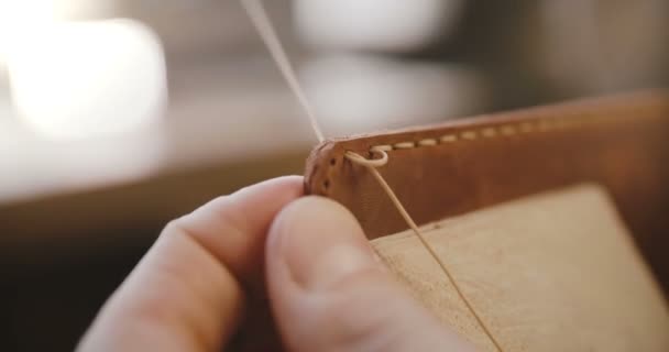 Macro plano plano de los detalles del proceso de costura de cuero, las manos con aguja y cuerdas haciendo una bolsa en la silla de montar en el taller — Vídeo de stock