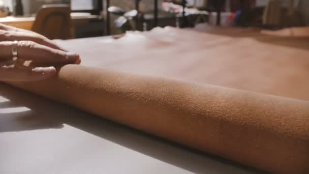 Κοντά shot της αρσενικό τεχνίτη χέρι τροχαίο ένα μεγάλο κομμάτι του καφέ δερμάτινο σε ένα ρολό στην κατασκευή πίνακα εργαστήρι. — Αρχείο Βίντεο