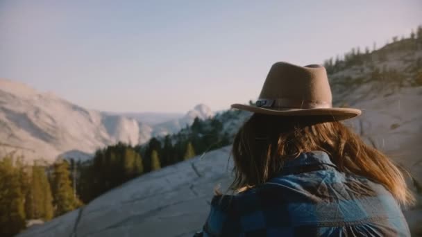 Vista trasera de una joven turista sentada sola en una roca observando una hermosa vista de la montaña en el parque nacional de Yosemite . — Vídeo de stock