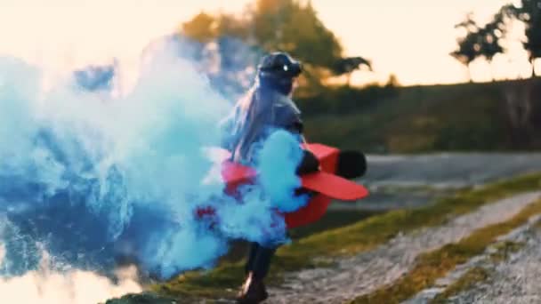 小快乐的飞行员女孩运行和旋转在有趣的纸板飞机与蓝色的颜色烟雾发挥飞行员慢动作 — 图库视频影像