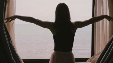 Kamera inanılmaz ocean view ağır çekim zevk için karanlık oda pencere perdeleri açmak için yürüyen genç güzel kadın izler.