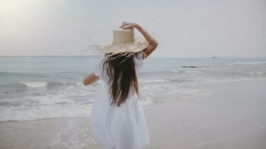 Saç ve sinematik tropikal egzotik okyanus plaj boyunca çalışan büyük hasır şapka uçan ile mutlu güzel 5-7 yıl yaşlı kız