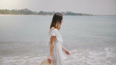 Yan görünümü şaşırtıcı genç güzel mutlu kadının rahatlatıcı ve dinlenme pastoral tropikal okyanus plaj boyunca yürüyüş vurdu.