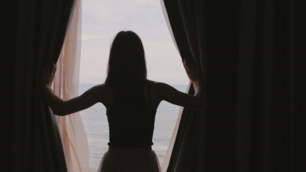 Joven mujer feliz abriendo cortinas de ventana en habitación oscura para disfrutar de increíbles vistas al mar, tocando el cabello en cámara lenta . — Vídeos de Stock