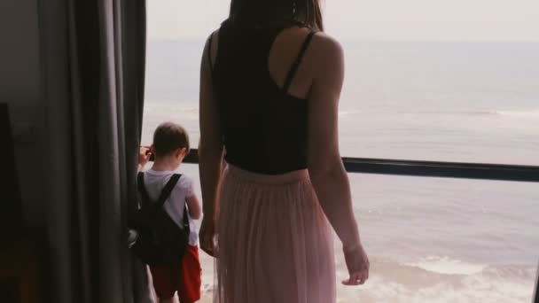 Joven madre con dos niños felices emocionados juntos en la gran ventana del apartamento viendo la increíble vista al mar en cámara lenta — Vídeos de Stock