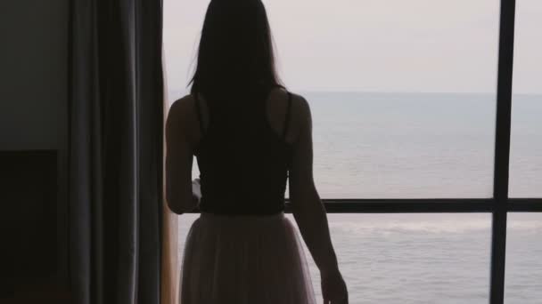 Young beautiful smiling woman traveler walking up to apartment window to enjoy incredible cloudy sea view slow motion. — Stock Video