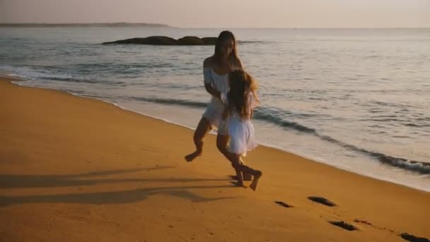 Happy beautiful young mother and little daughter playing and spinning together having fun at epic sunset ocean beach. — Stock Video