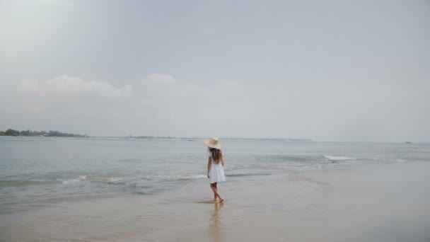 Geweldig achtergrond schot van gelukkig weinig 6-8 jaar oud meisje wandelen langs golven in ocean beach dragen grote stro hoed. — Stockvideo