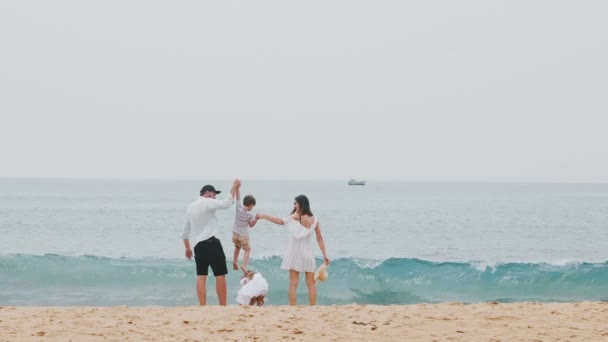 Šťastná rodina, mladý otec a matka Zvedněte své malé děti, drželi se za ruce, spolu s úsměvem na úžasné pláži moře. — Stock video