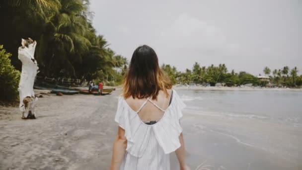 Slow motion close-up camera follows beautiful happy tourist woman walk along amazing tropical sea beach with straw hat. — Stock Video