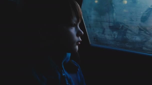 Atmosferische schot van 4-6 jaar oude thoughful Kaukasische jongetje kijken uit mistige autoruit in schemering donkere avond. — Stockvideo