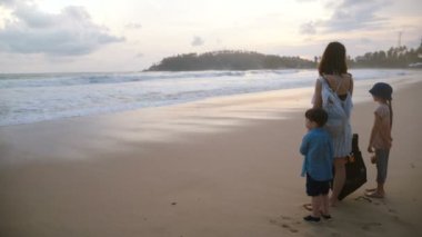 Arkadan Görünüm egzotik tropik deniz kumsalda inanılmaz atmosferik gün batımını izlemek iki çocuk birlikte mutlu genç anne.