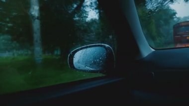 Sinematik orta atış, ağır yağmur altında Sri Lanka kasabanın içinden sürüş araba penceresi içinde yan ayna görünümü.