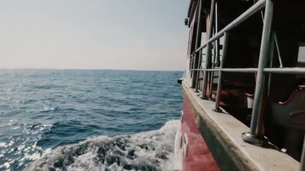 La cámara está en el lado izquierdo del barco de crucero navegando rápido en mar abierto, cortando olas azules espumosas en un día soleado claro . — Vídeos de Stock