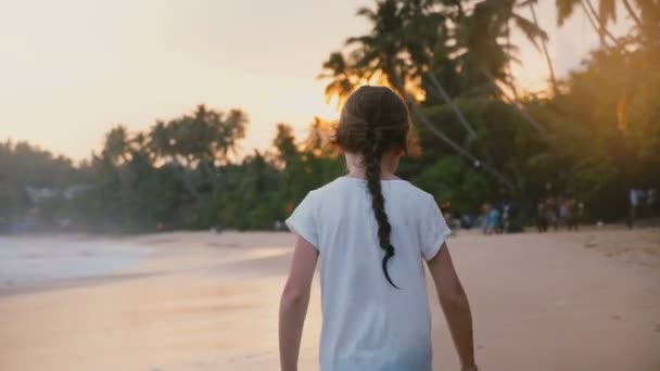 Camera volgt gelukkig ontspannen 5-7 jaar oud meisje kindje wandelen langs zonnige tropische zonsondergang zee strand op vakantie. — Stockvideo