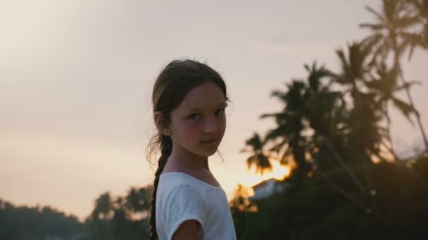 Happy relaxed little 6-8 years old female child looking back at camera, posing at sunset tropical sea beach on vacation. — Stock Video