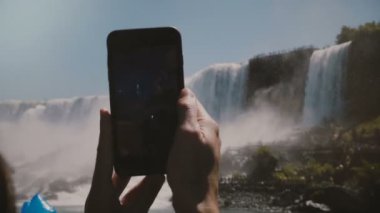 Yavaş hareket yakın çekim, insan elleri siyah Smartphone tutarak, epik Niagara Falls şelale sahne fotoğraf çekerken.