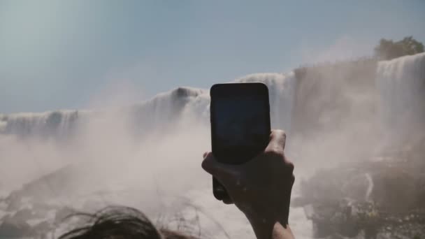 Slow motion close-up human hand holding big smartphone taking photos of incredible Niagara Falls waterfall panorama. — Stock Video