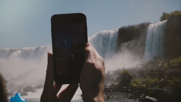 Повільний рух крупним планом постріл, людські руки проведення чорний смартфон, беручи фотографії епічного Ніагарського водоспаду пейзажі. — стокове відео